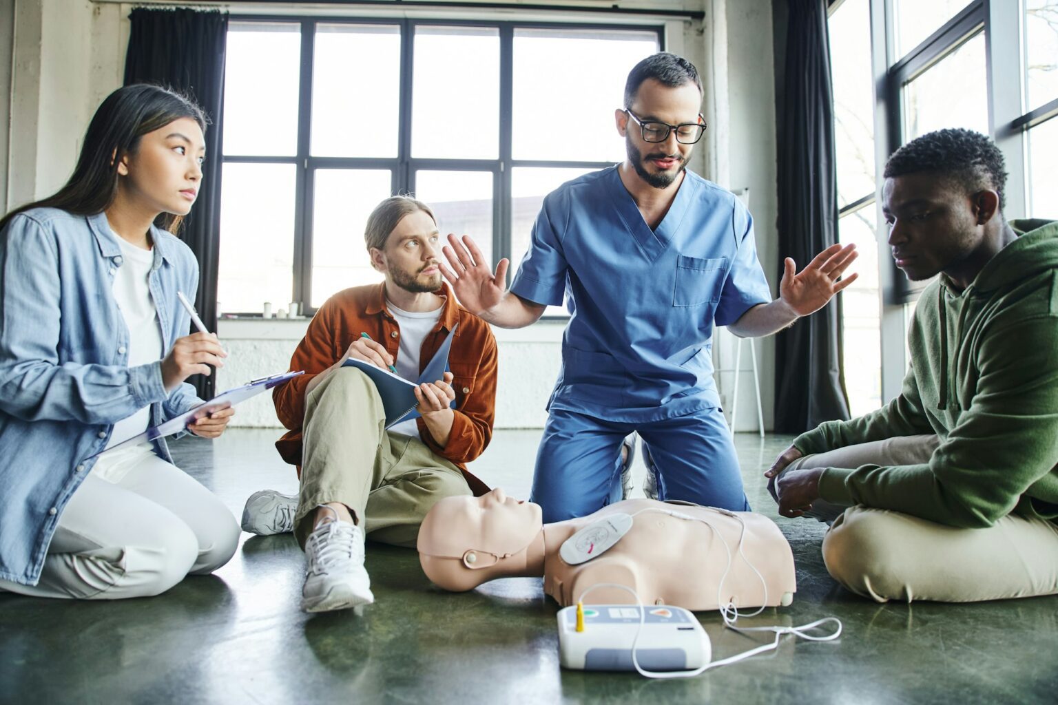 professional paramedic gesturing and talking to multiethnic participants near CPR manikin